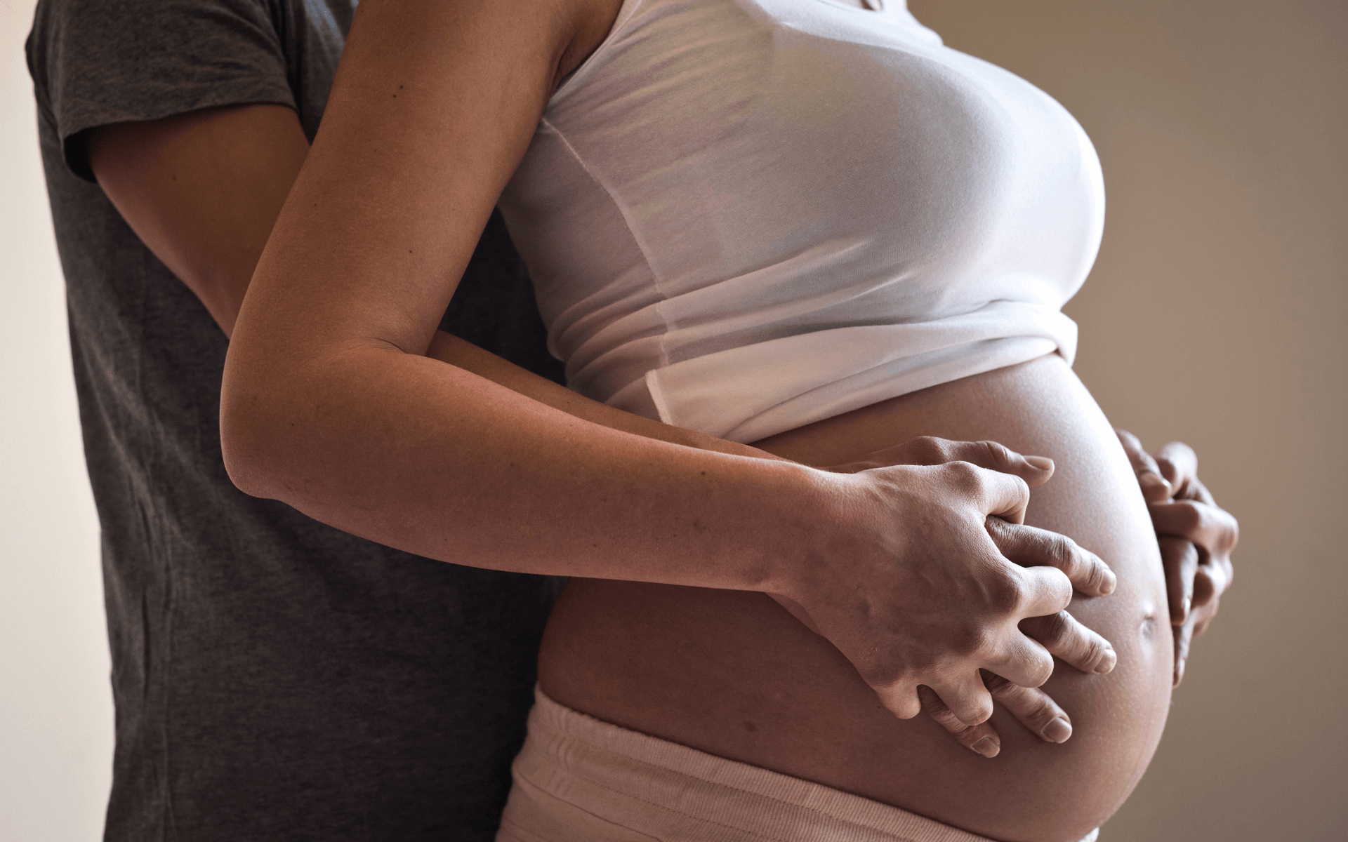 Gravid kvinne og mannlig partner holder hendene på den gravide magen