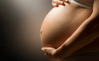 Gravid person i profil holder hendene på magen